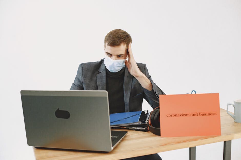 Stressed businessman in a face mask working remotely during COVID-19 pandemic.