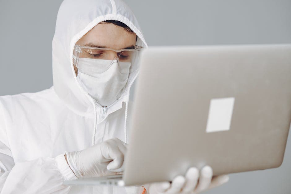 A healthcare worker in PPE using a laptop for remote work, symbolizing modern medicine and digital innovation.