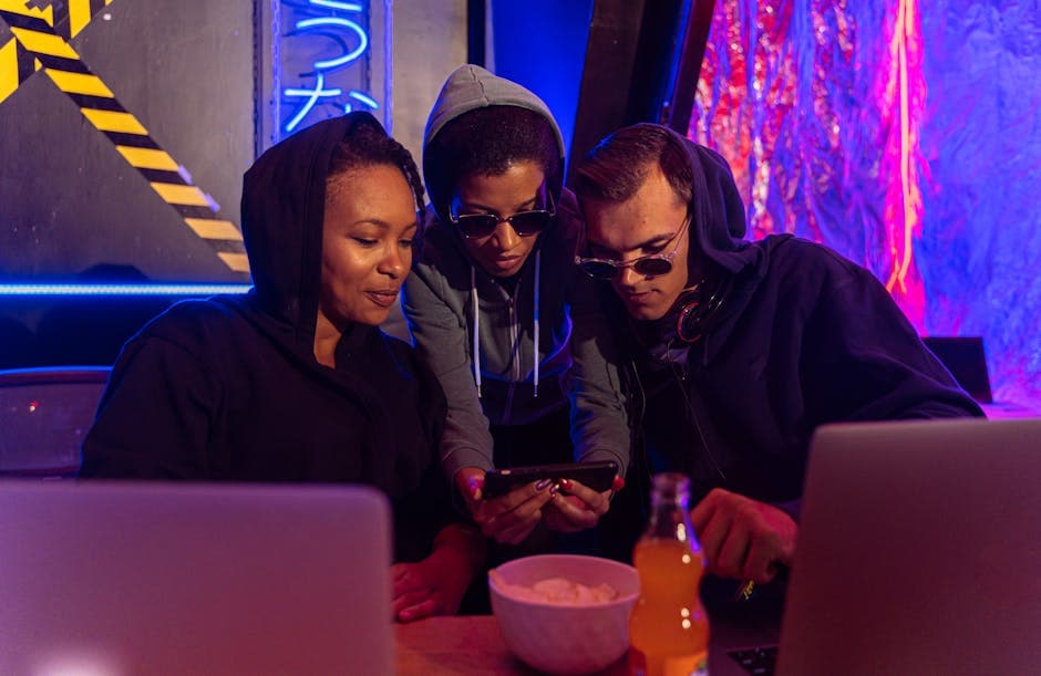 People in hoodies gathered in a cyber-themed bar using technology devices at night.