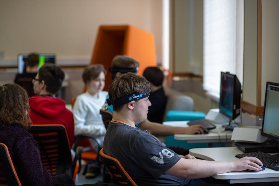 Group of teenagers engaged with computers and headsets in a modern classroom.