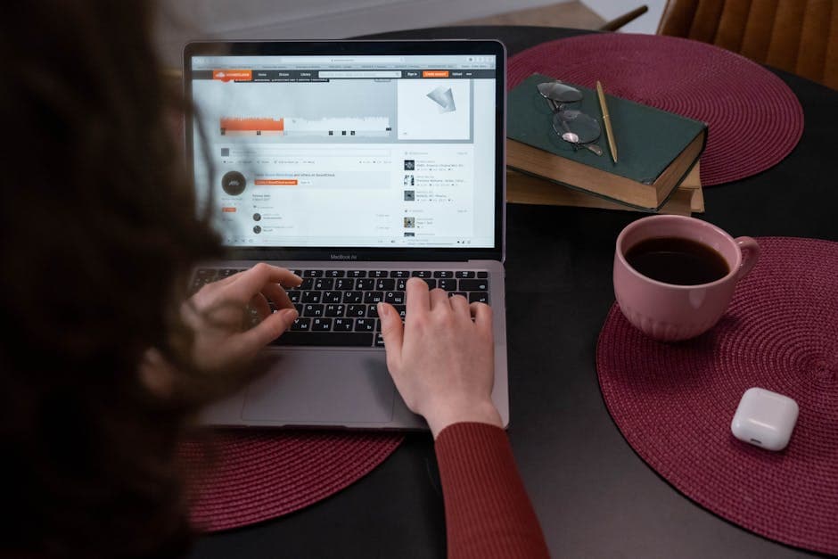 A woman types on a laptop while enjoying a cup of tea at her home workspace.