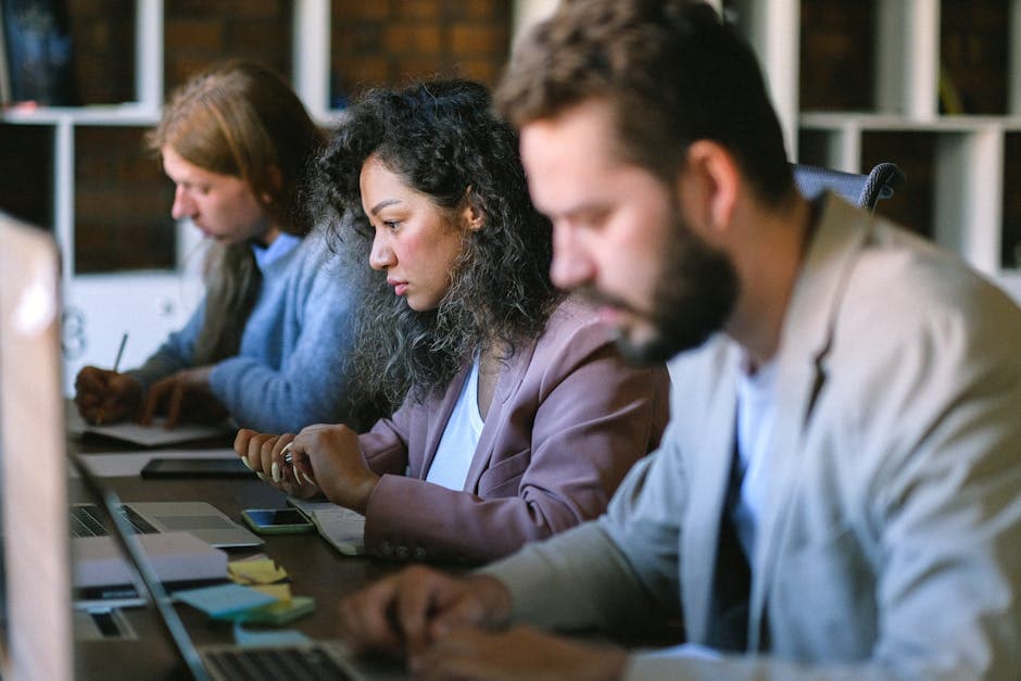 Concentrated serious coworkers browsing netbooks and writing in document while working together in modern workplace