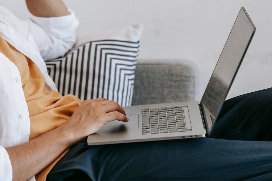 Side view of crop anonymous male sitting on sofa and using touchpad on laptop while browsing internet during free time at home
