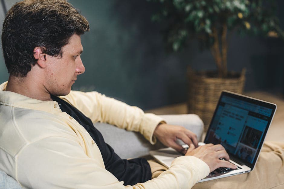 A young adult man deeply focused while working on a laptop indoors, sitting comfortably.