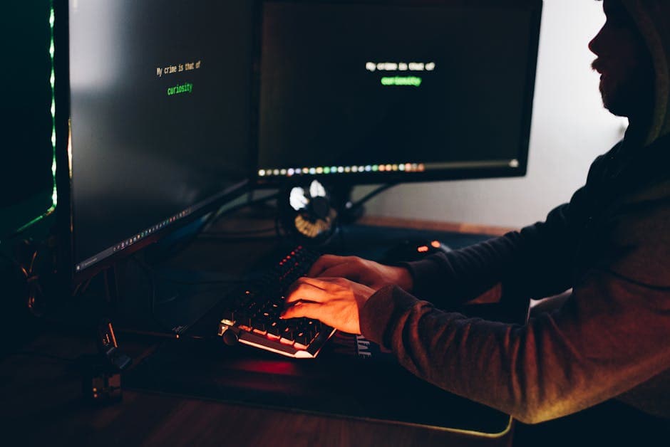 Side view of crop anonymous male cyber thief accessing information on desktop computer screens at dusk