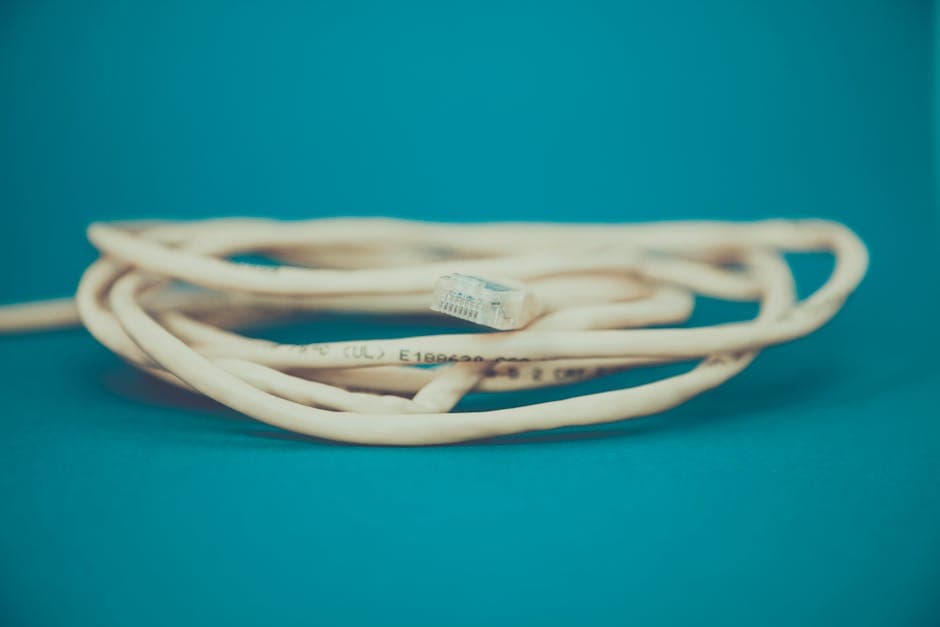 A detailed close-up of a coiled Ethernet cable with an RJ-45 connector against a teal background.