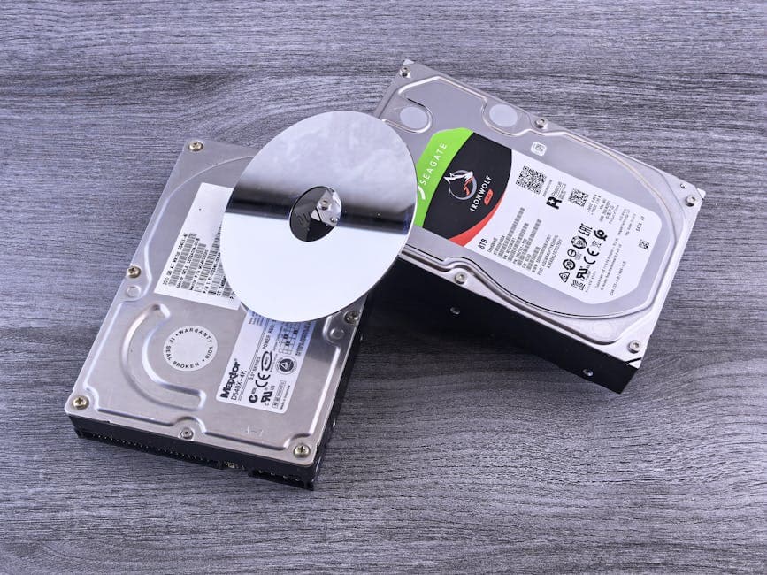 Two computer hard drives and a shiny disk displayed on a wooden surface.